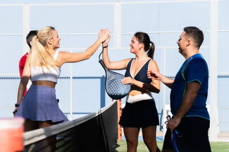 Friends high-fiving over the net during a padel match