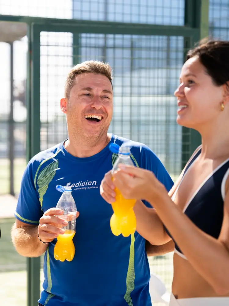 Dos compañeros riendo con bebidas tras un team building de pádel en Valencia